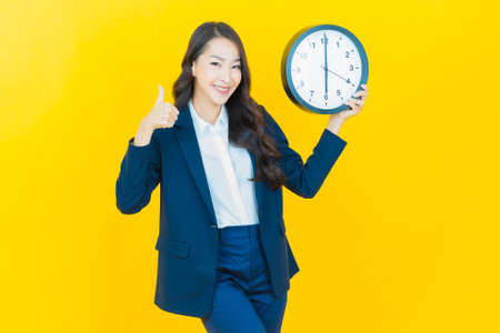 Portrait beautiful young asian woman show alarm or clock on yellow color background