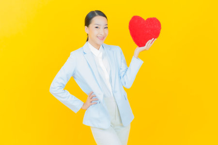 Portrait beautiful young asian woman smile with heart pillow shape on color backgroundの写真素材
