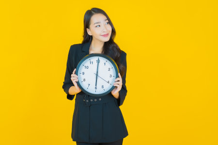 Portrait beautiful young asian woman show alarm or clock on yellow color backgroundの写真素材