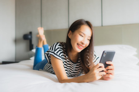 Portrait beautiful young asian woman use smart mobile phone in bedroom interiorの写真素材