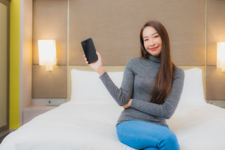 Portrait beautiful young asian woman use smart mobile phone on bed in bedroom interiorの写真素材