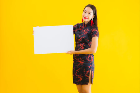 Portrait beautiful young asian woman wear chinese dress show white empty billboard for text in chinese new year concept on yellow isolated backgroundの写真素材