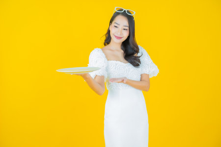 Portrait beautiful young asian woman smile with empty plate dish on color backgroundの写真素材