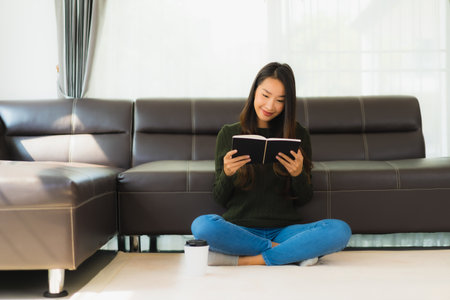 Portrait beautiful young asian woman read book with coffee cup and sofa in living room interiorの写真素材
