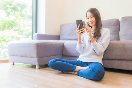 Portrait beautiful young asian woman use smart mobile phone on sofa in living room interiorの写真素材