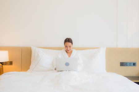 Portrait beautiful young asian woman use computer laptop on bed in bedroom interiorの写真素材