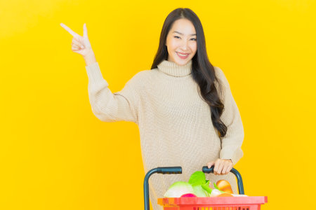Portrait beautiful young asian woman smile with grocery basket from supermarket on color backgroundの写真素材