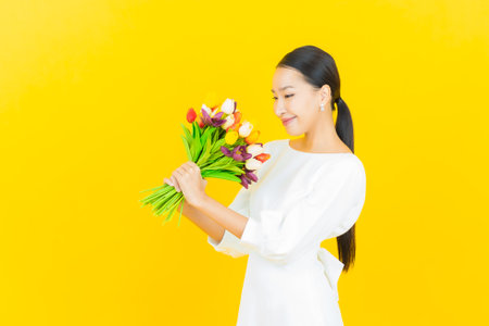 Portrait beautiful young asian woman smile with flower on yellow color backgroundの写真素材