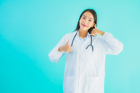 Portrait beautiful young asian doctor woman use mobile smart cell phone for clinic or hospital on blue isolated backgroundの写真素材