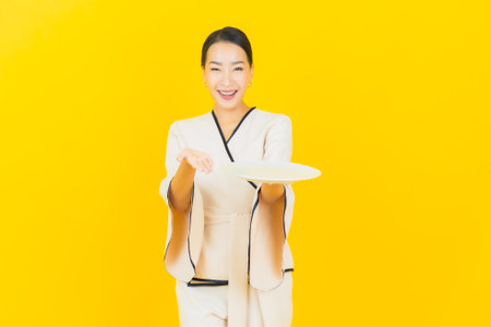 Portrait beautiful young business asian woman with empty dish plate on yellow backgroundの写真素材