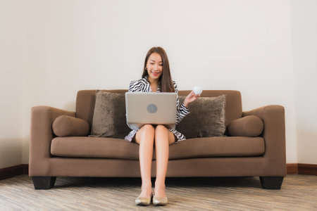 Portrait beautiful young asian woman use computer laptop on sofa in living room interior areaの写真素材