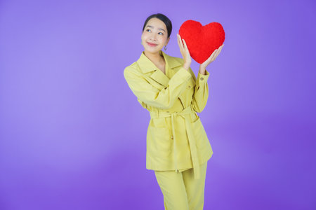 Portrait beautiful young asian woman smile with heart pillow shape on color backgroundの写真素材