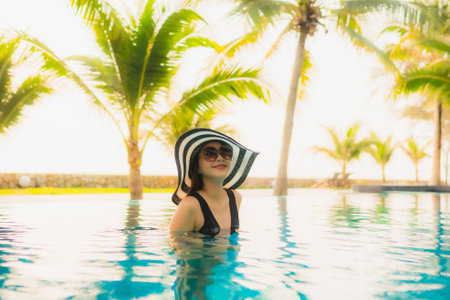 Portrait beautiful young asian woman relax around outdoor swimming pool in hotel resort with palm...