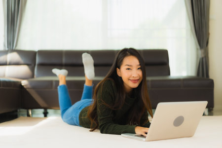 Portrait beautiful young asian woman use laptop computer with sofa in living room interiorの写真素材