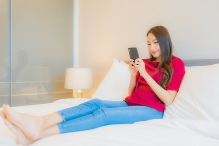 Portrait beautiful young asian woman use smart mobile phone on bed in bedroom interiorの写真素材