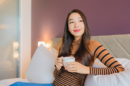 Portrait beautiful young asian woman with coffee cup on bed in bedroom interiorの写真素材