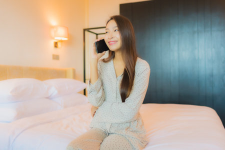 Portrait beautiful young asian woman on bed with smart mobile phone in bedroom interiorの写真素材