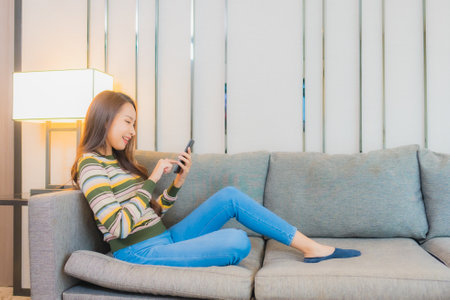 Portrait beautiful young asian woman use smart mobile phone on sofa in living room interiorの写真素材