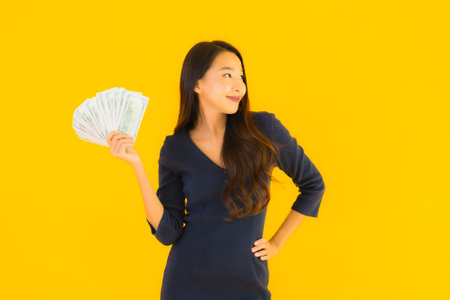 Portrait beautiful young asian woman with money and cash on yellow isolated backgroundの写真素材