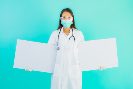 Portrait beautiful young asian doctor woman with empty card billboard banner on blue isolated backgroundの写真素材