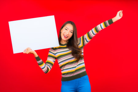 Portrait beautiful young asian woman with white empty billboard on red backgroundの写真素材