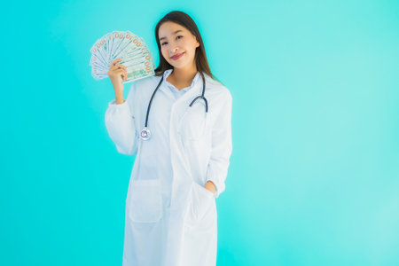 Portrait beautiful young asian doctor woman with a lot of cash and money on blue isolated backgroundの写真素材