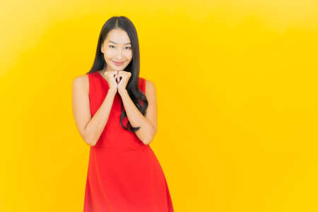 Portrait beautiful young asian woman wear red dress smile with action on yellow color backgroundの写真素材