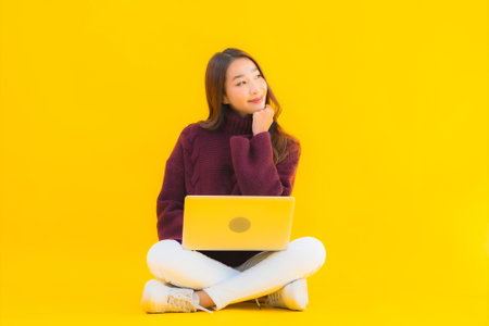 Portrait beautiful young asian woman use computer laptop on yellow isolated backgroundの写真素材