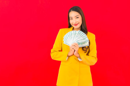 Portrait beautiful young asian woman with a lot of cash and money on red backgroundの写真素材