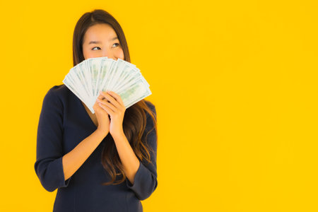 Portrait beautiful young asian woman with money and cash on yellow isolated backgroundの写真素材