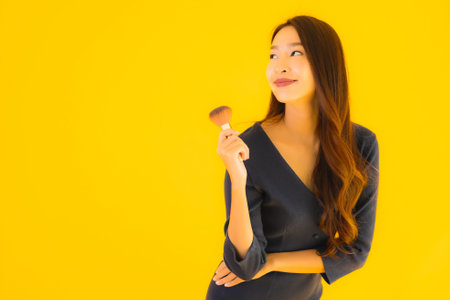 Portrait beautiful young asian woman with makeup brush on yellow isolated background