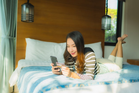 Portrait young asian woman using smart mobile phone with credit card for online shopping in bedroom interiorの写真素材