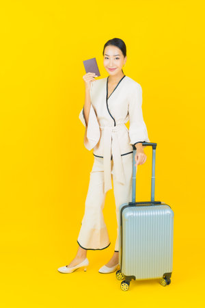 Portrait beautiful young business asian woman with luggage bag and passport ready for travel on yellow backgroundの写真素材