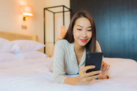 Portrait beautiful young asian woman on bed with smart mobile phone in bedroom interiorの写真素材