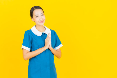 Portrait beautiful young asian woman maid and housekeeping smile with action on yellow color backgroundの写真素材