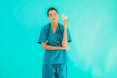Portrait beautiful young asian doctor woman with pill or drug and medicine on blue isolated backgroundの写真素材