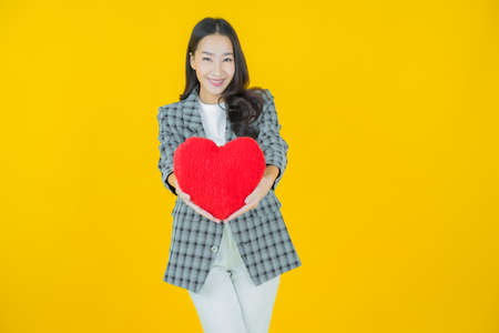 Portrait beautiful young asian woman smile with heart pillow shape on color backgroundの写真素材