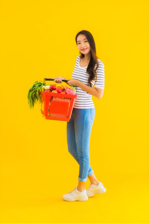 Portrait beautiful young asian woman with grocery basket cart from supermarket in shopping mall on yellow isolated backgroundの写真素材
