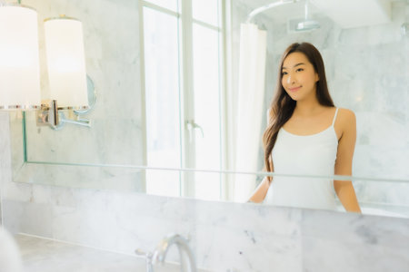 Portrait beautiful young asian woman check up and make up her face on mirror in bathroom interiorの写真素材