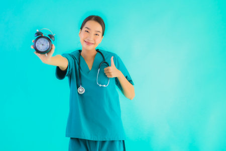 Portriat beautiful young asian doctor woman show clock or alarm on blue isolated backgroundの写真素材