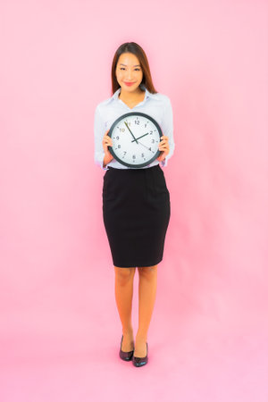 Portrait beautiful young asian woman show clock and alarm on pink backgroundの写真素材