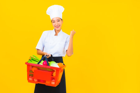 Portrait beautiful young asian chef woman with grocery basket from supermarket on yellow isolated backgroundの写真素材
