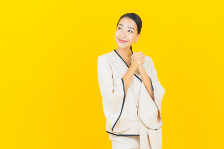 Portrait beautiful young business asian woman with smile and action yellow backgroundの写真素材