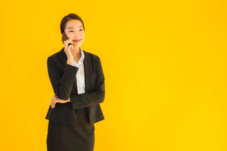 Portrait beautiful young business asian woman with smart mobile phone and coffee cup on yellow isolated backgroundの写真素材