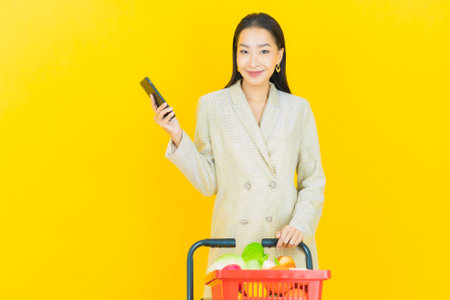 Portrait beautiful young asian woman smile with grocery basket from supermarket on color backgroundの写真素材