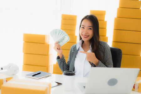 Portrait beautiful young asian woman work from home with laptop cash and cardboard box ready for shipping of online customer shoppingの写真素材