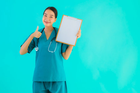 Portrait beautiful young asian doctor woman with empty paper board for copy space on blue isolated background - Healthcare in hospital and clinic conceptの写真素材