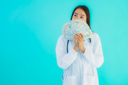 Portrait beautiful young asian doctor woman with a lot of cash and money on blue isolated backgroundの写真素材