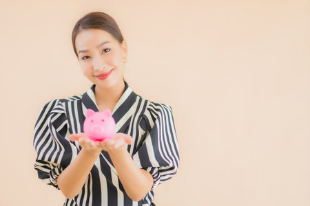 Portrait beautiful young asian woman with pink piggy bank on brown backgroundの写真素材