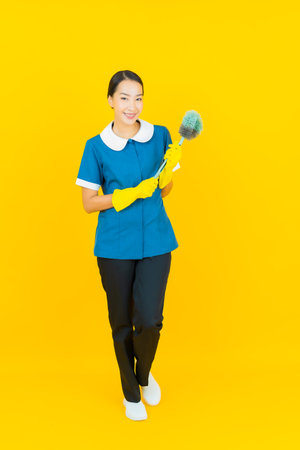 Portrait beautiful young asian woman maid and housekeeping smile with action on yellow color backgroundの写真素材